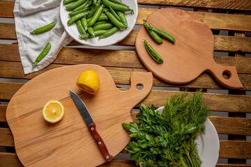 wooden table, wooden kitchen cutting board, pea pods, two halves of lemon, knifev