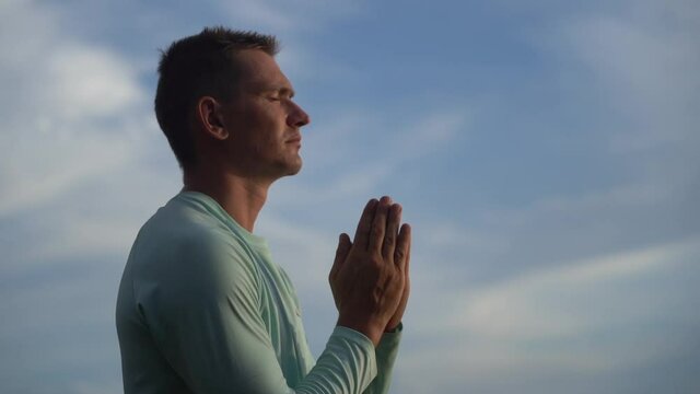 Young Man pray and cross oneself on blue sky background. Religion, faith and hope concept 