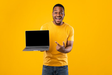 Excited African American Man Showing Laptop Blank Screen, Yellow Background