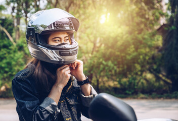 Confidence Asian woman wearing a motorcycle helmet before riding. Helmets contribute to motorcycle safety by protecting the rider's head. - obrazy, fototapety, plakaty