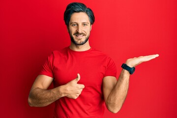 Young hispanic man wearing casual red t shirt showing palm hand and doing ok gesture with thumbs up, smiling happy and cheerful