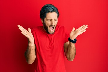 Fototapeta premium Young hispanic man wearing casual red t shirt celebrating mad and crazy for success with arms raised and closed eyes screaming excited. winner concept