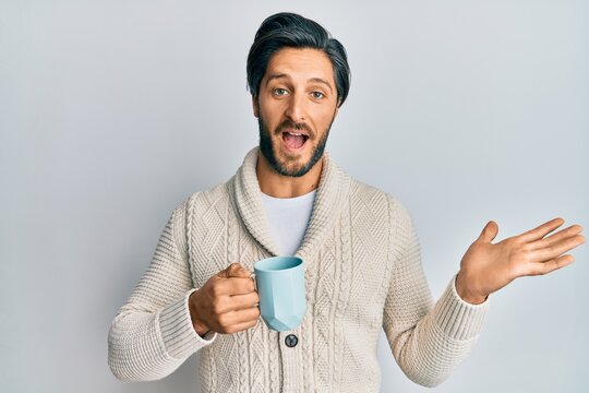 Young hispanic man drinking a cup of coffee celebrating achievement with happy smile and winner expression with raised hand