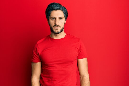 Young hispanic man wearing casual red t shirt relaxed with serious expression on face. simple and natural looking at the camera.