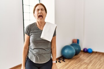 Middle age woman wearing sporty look training at the gym room angry and mad screaming frustrated...