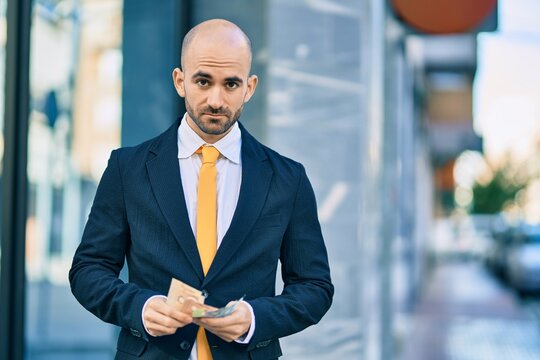 Young hispanic bald businessman with serious expression counting canadian dollars banknotes at the city.