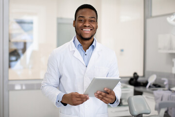 Obraz na płótnie Canvas Portrait of smiling handsome black dentist doctor with digital tablet in hands