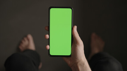 POV top view shot of man show phone with green screen indoor sitting on a couch