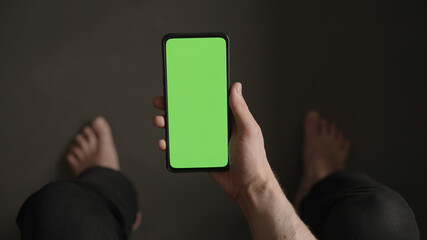 POV top view shot of man show phone with green screen indoor sitting on a couch