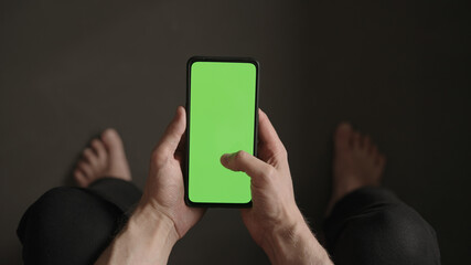 POV top view shot of man use phone with green screen indoor sitting on a couch