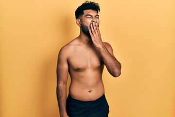 Fototapeta premium Arab man with beard wearing swimwear shirtless bored yawning tired covering mouth with hand. restless and sleepiness.