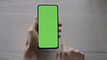 Man using phone with green screen on white oak table