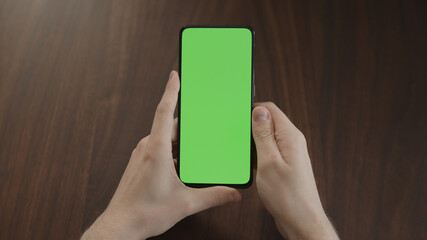 Man using phone with green screen on black wwalnut table
