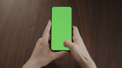 Man using phone with green screen on black wwalnut table