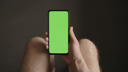 Man using phone with green screen while sitting with naked legs