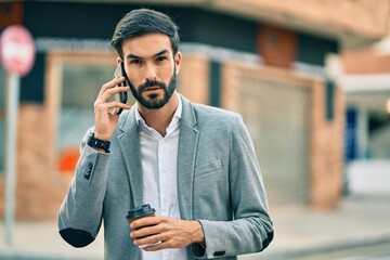 Young hispanic businessman with serious expression talking on the smartphone and drinking coffee at the city.