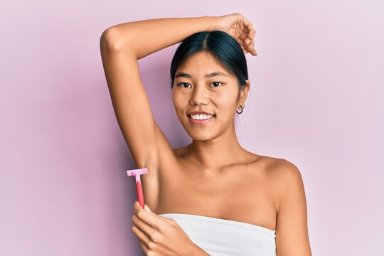 Young chinese woman wearing shower towel using razor smiling with a happy and cool smile on face. showing teeth.