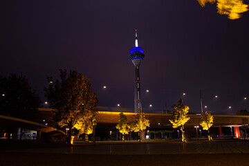 Der düsseldorfer Fernseherturm mit gelb beleuchteten Bäumen bei Nacht