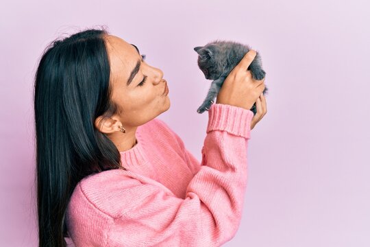 Young hispanic girl smiling happy holding cute cat over isolated pink background.