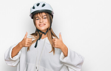Teenager caucasian girl wearing bike helmet success sign doing positive gesture with hand, thumbs up smiling and happy. cheerful expression and winner gesture.