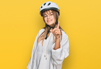 Teenager caucasian girl wearing bike helmet showing and pointing up with finger number one while smiling confident and happy.