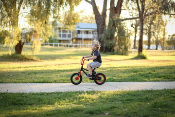 Little boy riding bike along walking track in pretty Australian bush setting at sunset