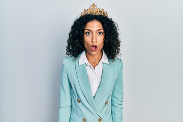Young latin girl wearing business clothes and queen crown scared and amazed with open mouth for surprise, disbelief face