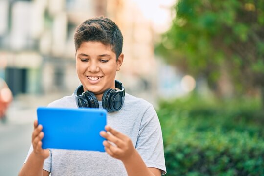 Adorable latin boy smiling happy using headphones and touchpad at the park.