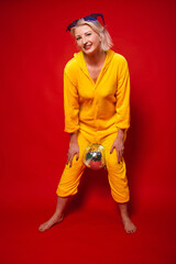 A bright girl at a party in purple big glasses in the form of stars and in yellow camisole pajamas. Funny and cheerful woman with a disco ball in her hands. Studio photo on red