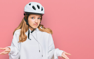 Beautiful young caucasian girl wearing bike helmet clueless and confused expression with arms and...
