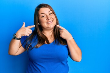 Fototapeta premium Beautiful brunette plus size woman wearing casual blue t shirt smiling cheerful showing and pointing with fingers teeth and mouth. dental health concept.