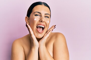 Beautiful brunette woman standing topless wearing face cream smiling and laughing hard out loud because funny crazy joke.