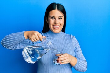 Beautiful brunette woman pouring water in glass smiling with a happy and cool smile on face. showing teeth.