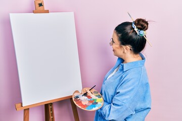 Young beautiful painter woman standing by easel with blank empty canva