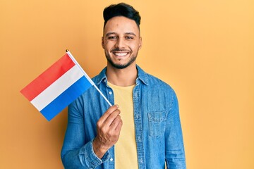 Young arab man holding holland flag looking positive and happy standing and smiling with a...