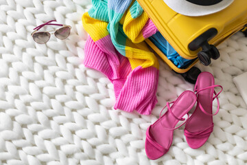 Top view yellow suitcase with necessary things preparing to summer travel vacation on knitted plaid