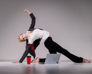 A ballerina dressed in a business suit poses for a laptop and drinks coffee. Flexible woman works...