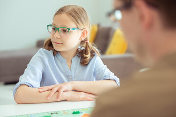 Portrait of pretty teen girl in glasses playing board game with parents
