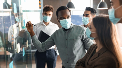 Workers in masks having meeting using sticky post-it notes