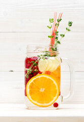 Summer detox infused lemonade with fruits and berries in glass jar on white wooden background