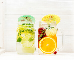 Summer cold infused lemonade with fruits and berries in glass jars on white wooden background
