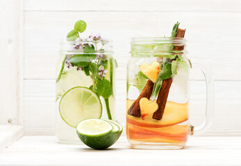 Summer infused detox .cold waters with limes, peaches and mint in glass jars mason on white wooden background