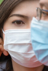 Portrait of Asian couple wearing protective masks in vertical frame, focus at woman's face looking at camera with blurred side of man's face on foreground