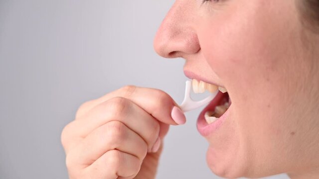 Caucasian woman brushing teeth with toothpick with dental floss on white background.