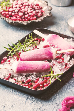 pink cranberry popsicle with rosemary and berries on ice over vintage background.