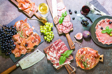 Different types jamon on cutting boardes with figs, grapes and wine. Parma ham hamon on wooden background with copy space, top view.