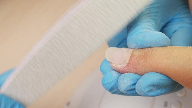 Nail master shapes the nails with a nail file. Nail file processing. Manicurist files the shape of the nails with a special nail file, close up view.  Process of nail care in a beauty salon. Closeup
