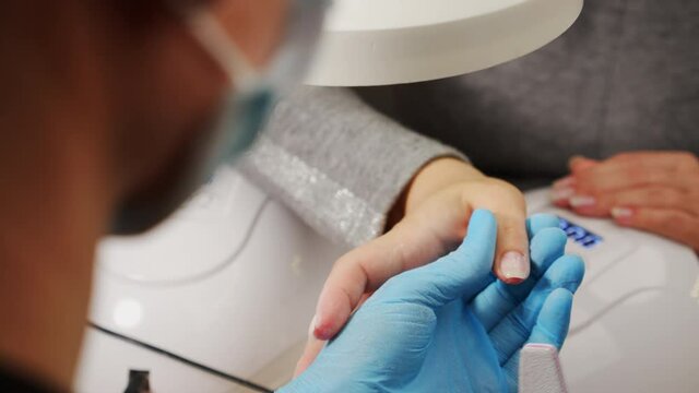 Manicurist files the shape of the nails with a special nail file, close up view. The manicurist shapes the nails with a nail file. The process of nail care in a beauty salon. Nail file processing.
