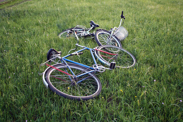 Two bicycles lie on a green slope against the background of the sunset.