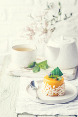 Piece of mango mousse cake on plate over white wooden table.